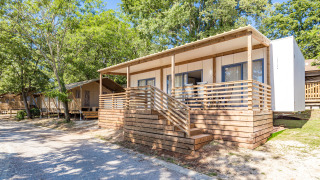 Das Mobile Home Pula mit Holzterrasse im Grünen, umgeben von Bäumen und Natur in sonniger Lage.