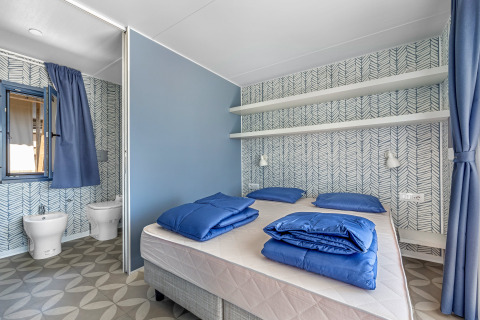 Schlafzimmer im Mobile Home Pula auf Camping Bijela Uvala in Kroatien mit moderner Einrichtung und blauer Bettwäsche.