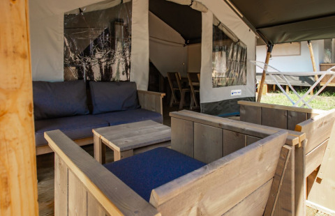 Zona de estar con muebles de madera y cojines azules en la Safari Tent Comfort en Camping Bijela Uvala, Croacia.