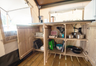 Åben køkkenskab i en safaritelt på Camping Bijela Uvala i Kroatien, med gryder, glas og køkkenudstyr.