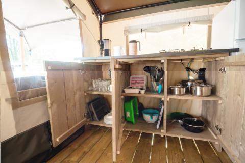 Armario de cocina abierto en una tienda safari en Camping Bijela Uvala, Croacia, con ollas y utensilios.