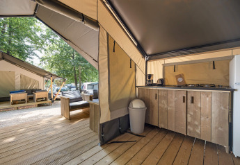 Vista interna di una tenda safari moderna con angolo cucina, mobili in legno e una seconda tenda fuori.