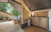 Interior view of a modern safari tent featuring a kitchenette, wooden furniture, and another tent outside.