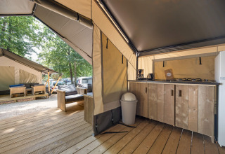 Binnenaanzicht van een moderne safaritent met keukenblok, houten meubels en een tweede tent buiten.