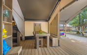 Intérieur d'une tente safari avec table en bois, bancs, et vue sur la terrasse et la nature extérieure.