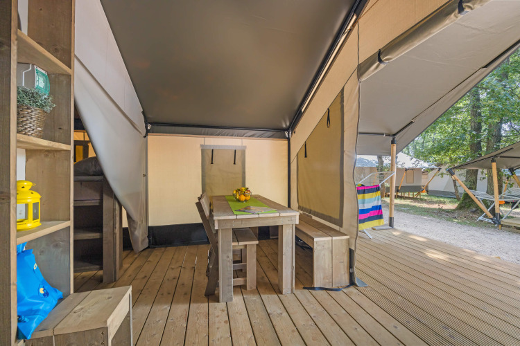 Interior de una tienda safari con mesa de madera y bancos, vista abierta a la terraza y naturaleza.