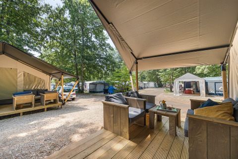 Camping en tienda safari con terraza de madera, asientos cómodos y vista a otras tiendas y árboles.