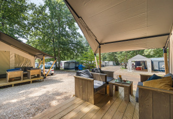 Camping en tienda safari con terraza de madera, asientos cómodos y vista a otras tiendas y árboles.