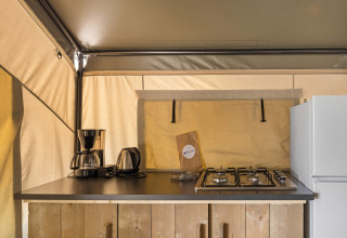 Petite cuisine dans une tente safari avec cafetière, bouilloire, gazinière et réfrigérateur.