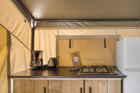 Keukentje in een safaritent met koffiezetapparaat, waterkoker, gasfornuis en koelkast.