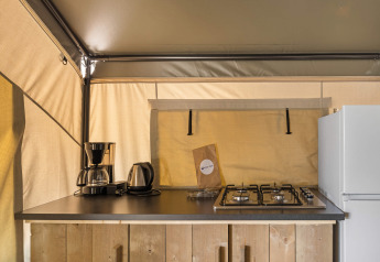 A kitchenette inside a safari tent featuring a coffee maker, kettle, gas stovetop, and refrigerator.