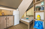 Innenaufnahme eines Safarizelts mit Holzboden, Kochnische, Kühlschrank und Doppelbett.
