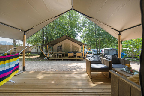 Vue d’une terrasse de tente safari avec coin salon extérieur donnant sur d’autres tentes en plein bois.