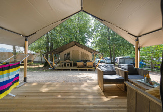 View from a safari tent patio with outdoor seating, looking toward other tents in a wooded campsite.