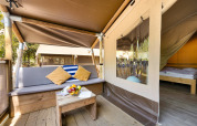 Eingang zur Safari Tent Lodge mit Außenbereich, Sitzbank, Kissen und Blick ins gemütliche Schlafzimmer.