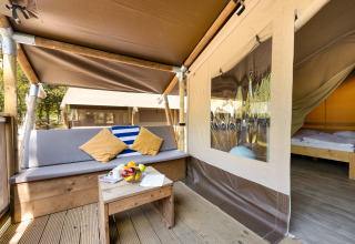 Entrada a Safari Tent Lodge con zona de estar exterior, cojines coloridos y vista al dormitorio interior.
