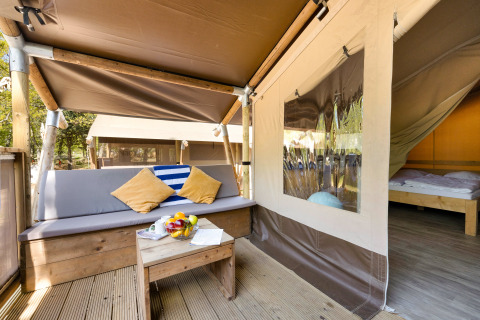 Eingang zur Safari Tent Lodge mit Außenbereich, Sitzbank, Kissen und Blick ins gemütliche Schlafzimmer.