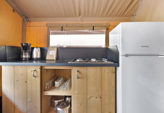 Pequeña cocina en Safari Tent Lodge con cafetera, hervidor, estufa, vasos y un refrigerador blanco.