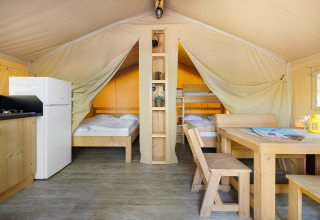 Interior de la Safari Tent Lodge con muebles de madera, cama doble, litera, cocina y mesa de comedor.