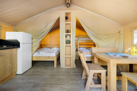Interieur van Safari Tent Lodge met houten meubels, tweepersoonsbed, stapelbed, keuken en eettafel.