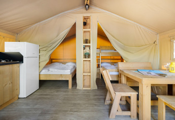 Indretning af Safari Tent Lodge med træmøbler, dobbeltseng, køjeseng, køkken og spisebord.