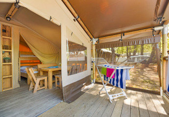Interior de Safari Tent Lodge con muebles de madera, camas, tendedero y vistas al bosque exterior.