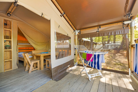 Safari Tent Lodge mit Holzmöbeln, Schlafbereich, Wäscheständer und Blick auf die bewaldete Umgebung.