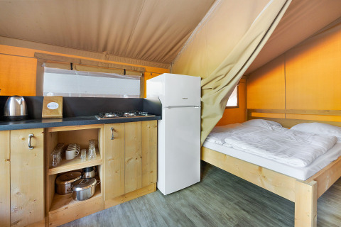 Vista interna della Safari Tent Lodge con cucina in legno, fornello a gas, frigorifero e letto matrimoniale.