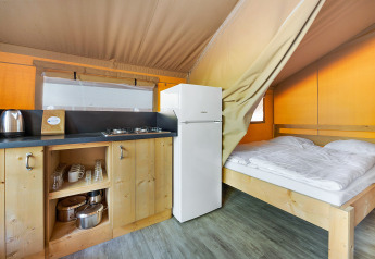 Vista interna della Safari Tent Lodge con cucina in legno, fornello a gas, frigorifero e letto matrimoniale.