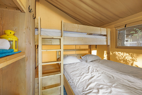 Interno della Safari Tent Lodge con letto a castello, letto matrimoniale, scaffali in legno e luce naturale.