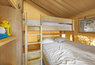 Interior de la Safari Tent Lodge con dos literas, cama doble, estantes de madera y luz natural.