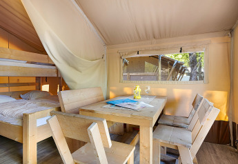 Interno di una Safari Tent Lodge con mobili in legno, tavolo da pranzo e letti a castello alla luce naturale.