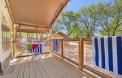 Houten terras met droogrek en gestreepte handdoeken bij Safari Tent Lodge omgeven door bomen en zon.