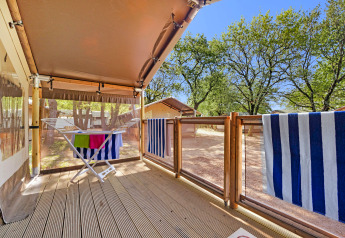 Houten veranda met droogrek en gestreepte handdoeken bij Safari Tent Lodge, omgeven door bomen.