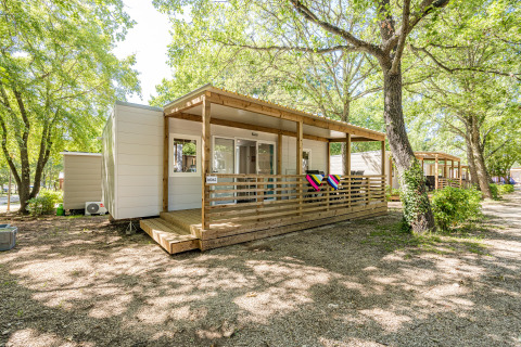 Mobil-home Fuskulin au Camping Bijela Uvala en Croatie, entouré d’arbres et d’une terrasse en bois.