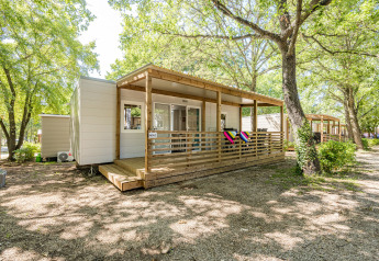 Mobile home Fuskulin at Camping Bijela Uvala in Croatia, surrounded by trees and featuring a wooden porch.