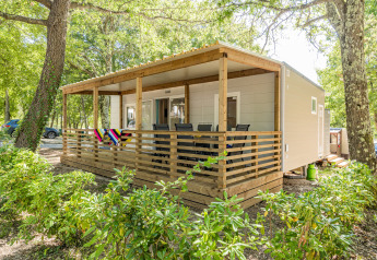 Mobil-home Fuskulin au Camping Bijela Uvala en Croatie, avec terrasse couverte, entouré d’arbres verdoyants.