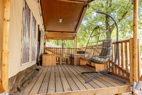 Terrazza in legno con sedia sospesa e area salotto davanti a tenda safari climatizzata a Camping Bijela Uvala, Croazia.