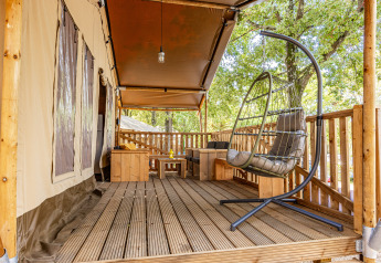 Terrazza in legno con sedia sospesa e area salotto davanti a tenda safari climatizzata a Camping Bijela Uvala, Croazia.