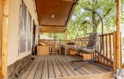 Wooden terrace with hanging chair and outdoor seating at safari tent with AC at Camping Bijela Uvala, Croatia.