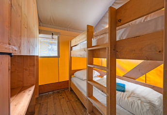 Interno di tenda safari con letti a castello in legno, finestra e ripostiglio al Camping Bijela Uvala, Croazia.