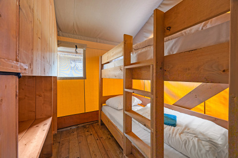 Interno di tenda safari con letti a castello in legno, finestra e ripostiglio al Camping Bijela Uvala, Croazia.