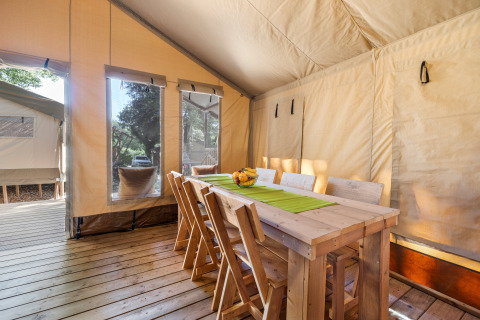 Zona pranzo in tenda safari con tavolo e sedie in legno, luce solare e finestre a Camping Bijela Uvala, Croazia.