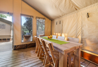 Zona pranzo in tenda safari con tavolo e sedie in legno, luce solare e finestre a Camping Bijela Uvala, Croazia.