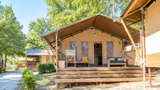 Safari-Zelt mit Terrasse, Klimaanlage und Sanitäranlagen, umgeben von Bäumen und Natur im Sonnenlicht.