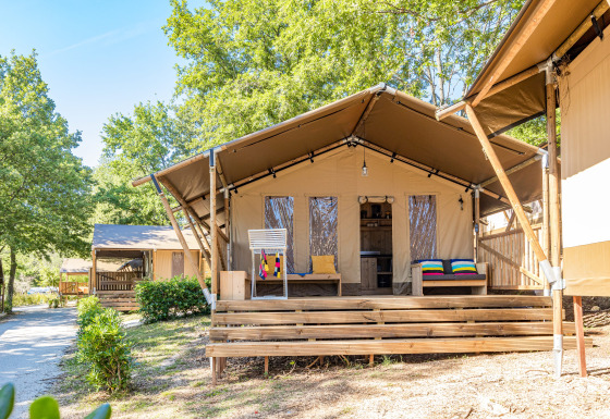 Tente safari avec terrasse, climatisation et sanitaires privés, entourée d’arbres et de verdure.