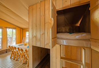 Interior de tienda safari en Camping Bijela Uvala, Croacia, con comedor y cama empotrada acogedora.