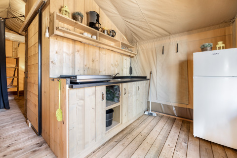 Zona cucina interna con pannelli di legno, mensole, frigo e fornello in una tenda safari a Camping Bijela Uvala.