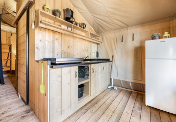 Zona cucina interna con pannelli di legno, mensole, frigo e fornello in una tenda safari a Camping Bijela Uvala.