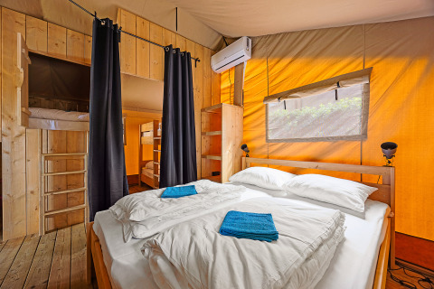 Vista interna di una tenda safari con letto matrimoniale, letti a castello, aria condizionata e arredo in legno in Croazia.